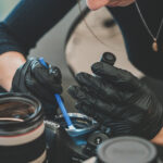 Person examining and cleaning used camera lenses wearing black gloves