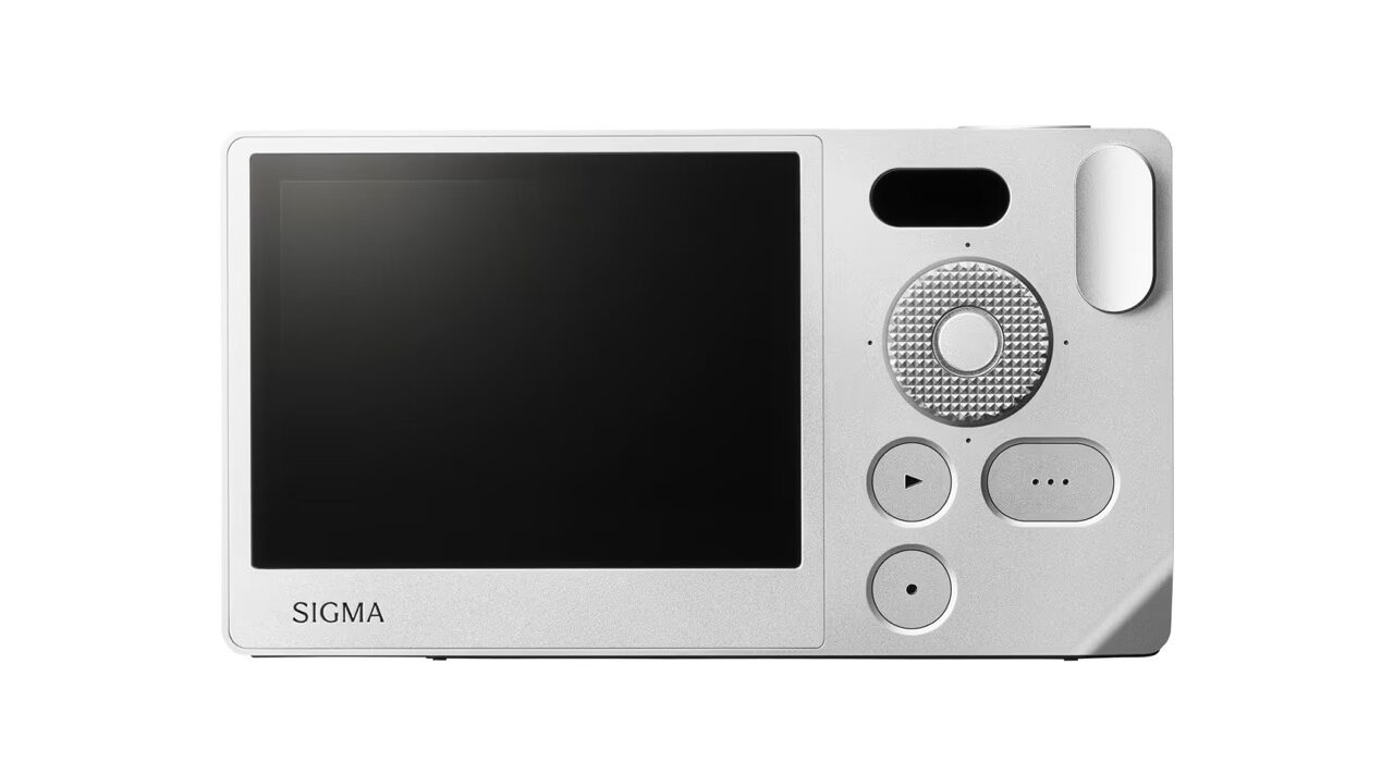 A white mirrorless camera. Rectangle device with a large screen and some dials