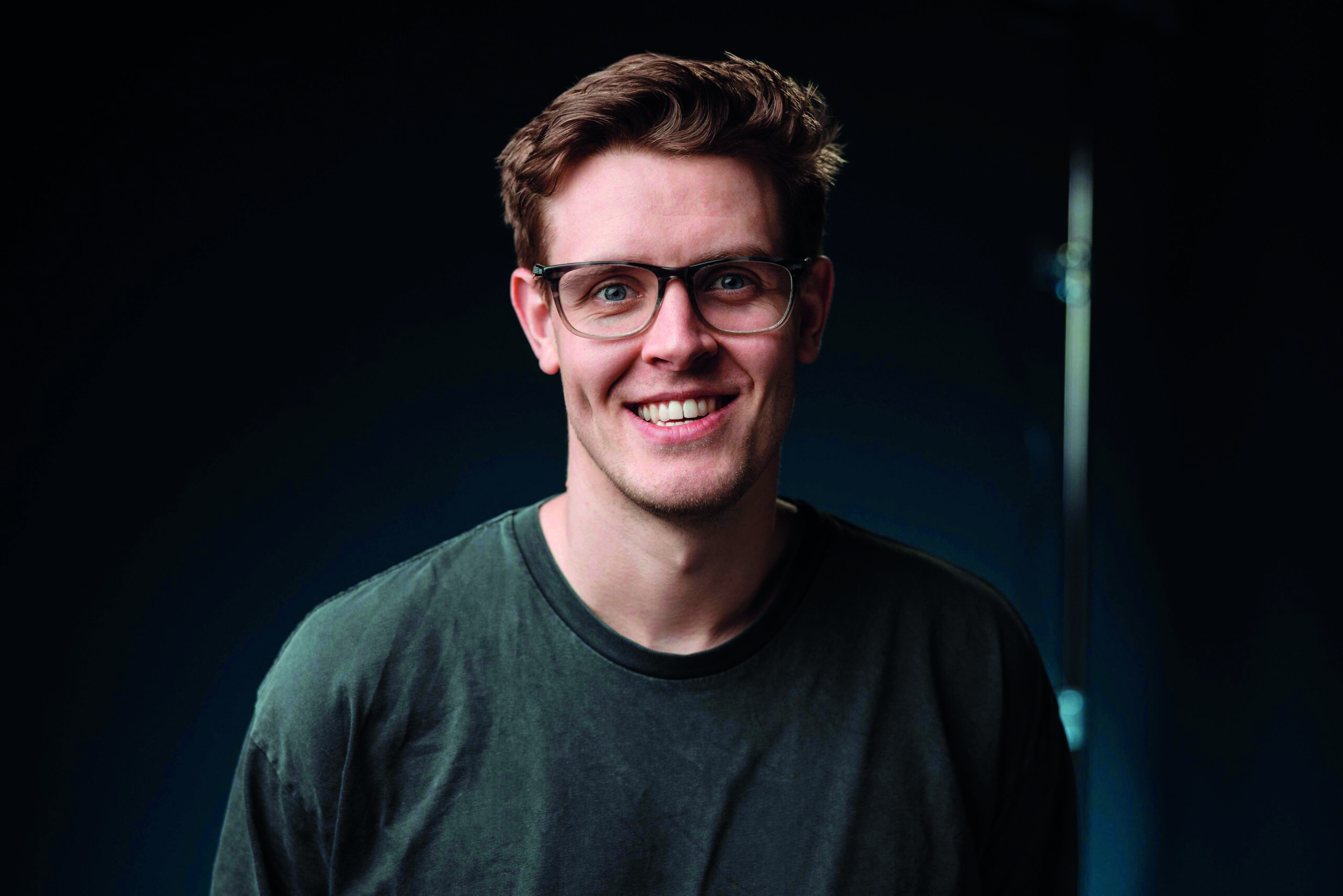 A man wearing a green top and glasses, smiling at the camera