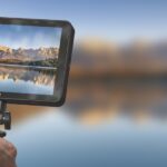 A device with a screen showing a mountain and lake landscape. The same mountain and lake is blurred in the background