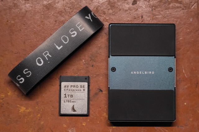 A band laying on a table holding next to a 1TB card and a black rectangle on a brown table