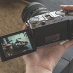 A person holding a Fujifilm X-M5 camera and taking photos of food on a table